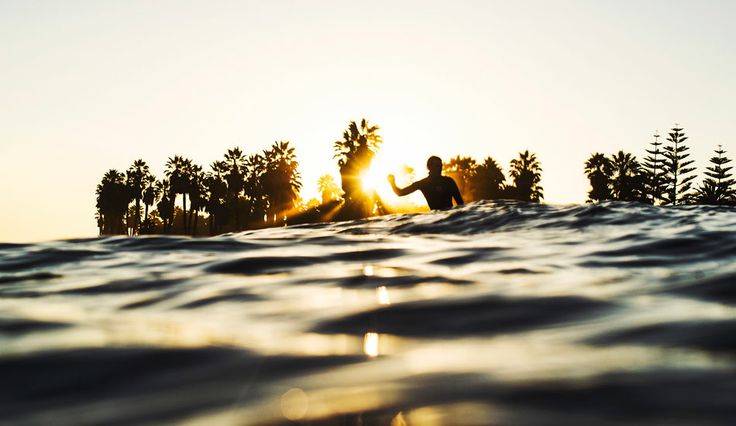 A surfer backlit by a setting sun, shot from behind the wave