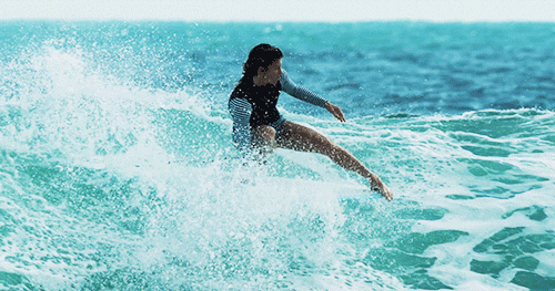 a gif of Leah Dawson grabbing the rail of her surfboard while hanging five