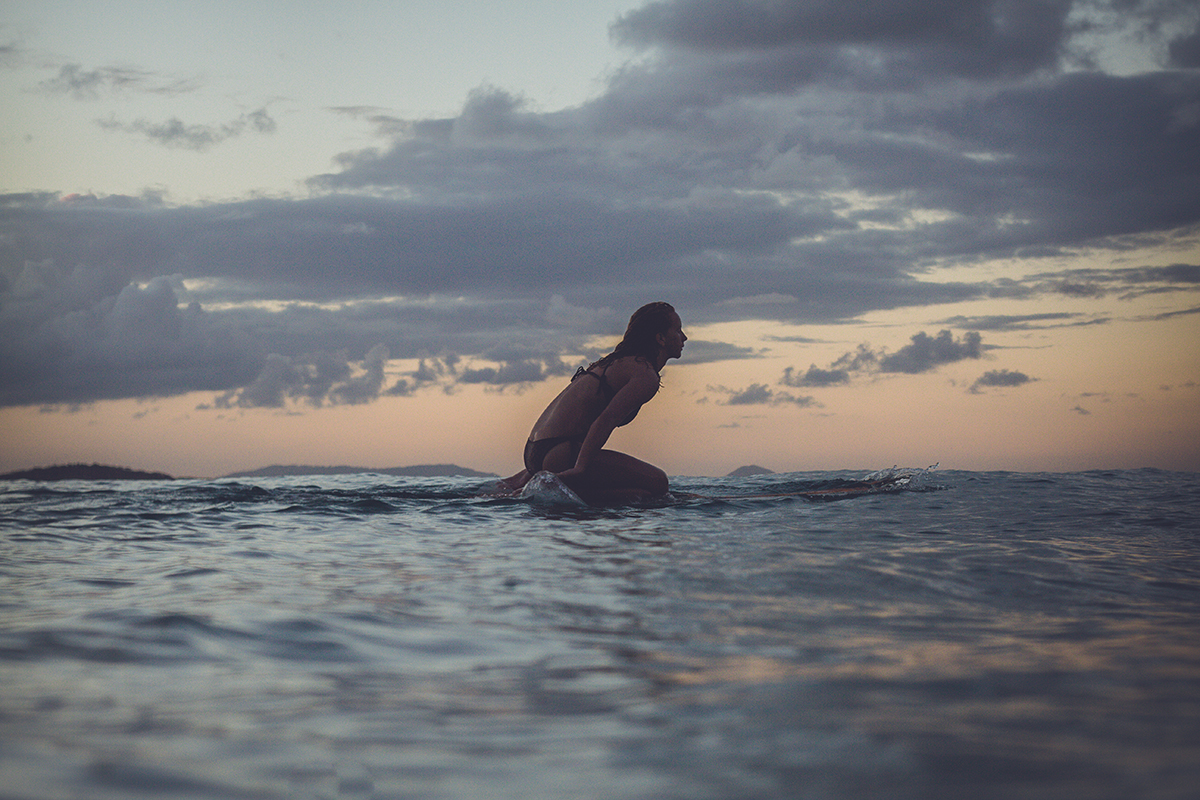 An image of Surfer Margaux Arramon-Tuccoo knee paddles her surfboard under a cloudy sky