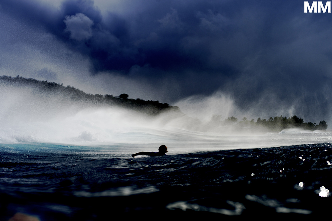 An image of a surfer paddles behind a breaking wave