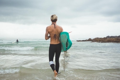 A woman wades into the ocean, surfboard tucked under her arm